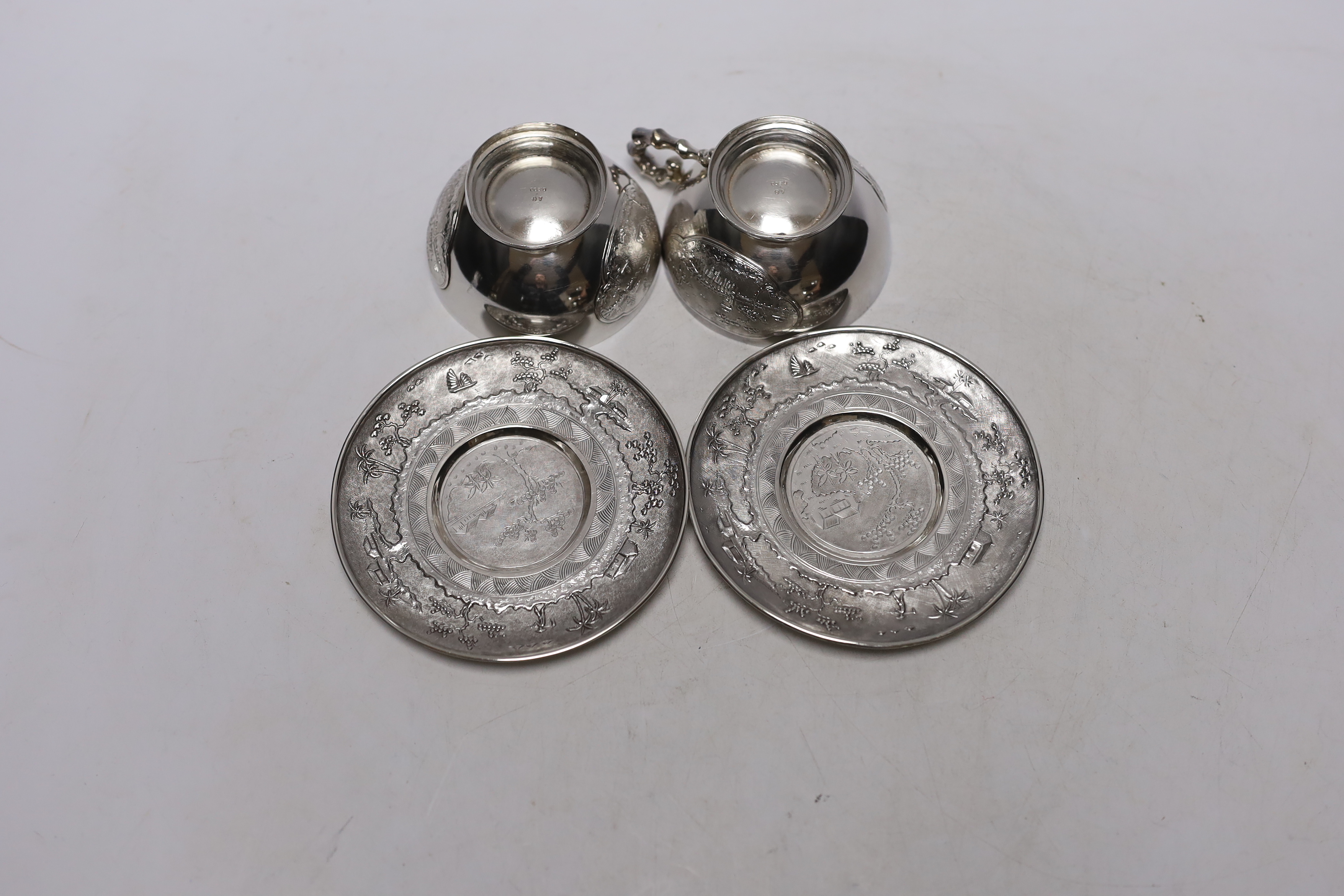 Two early 20th century Vietnamese 800 standard white metal tea cups and saucers (one lacking handle), saucer diameter 10.1cm, 6.6oz.